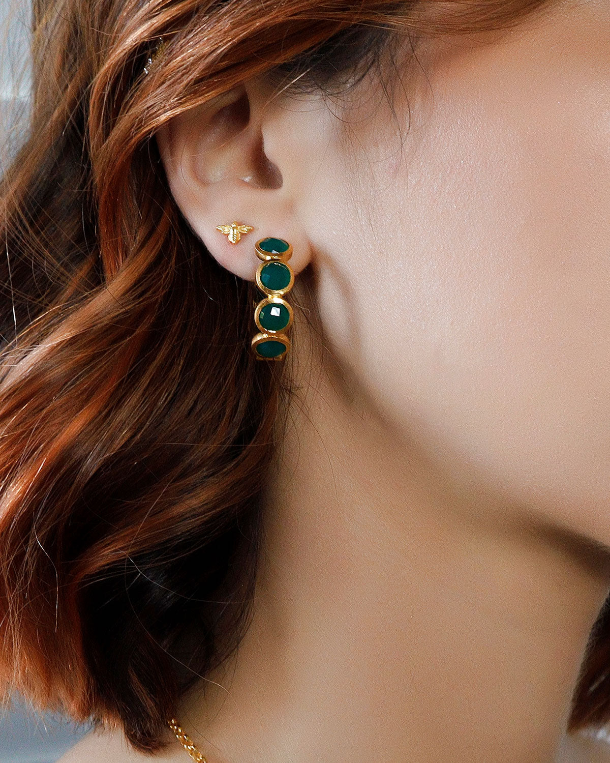 Close-up of gold hoops with emerald green gemstones and smooth polish