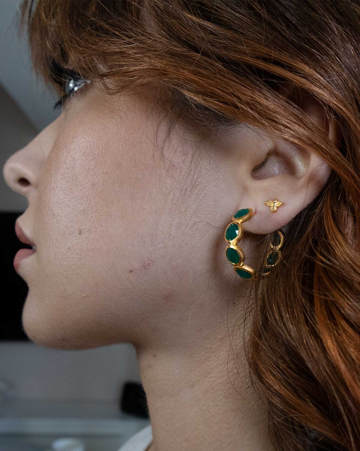 Model wearing small gold hoop earrings with emerald green gemstones