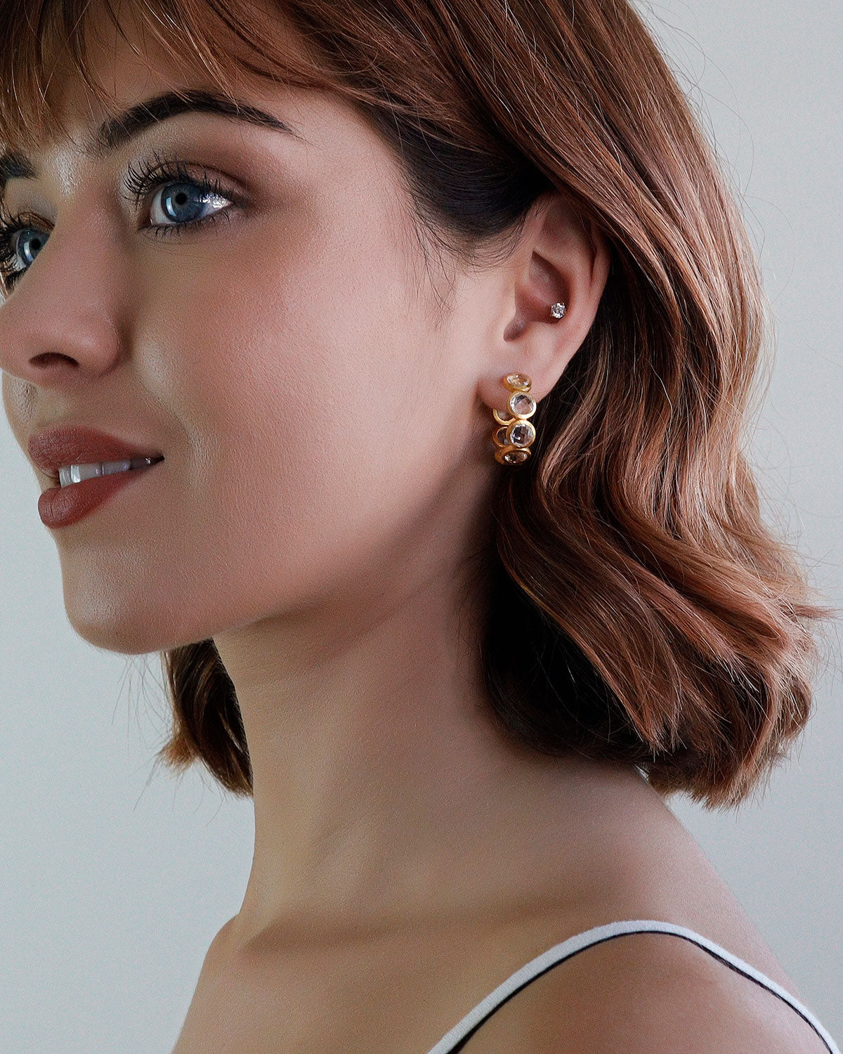 Model wearing midsize gold hoops with natural crystal gemstones