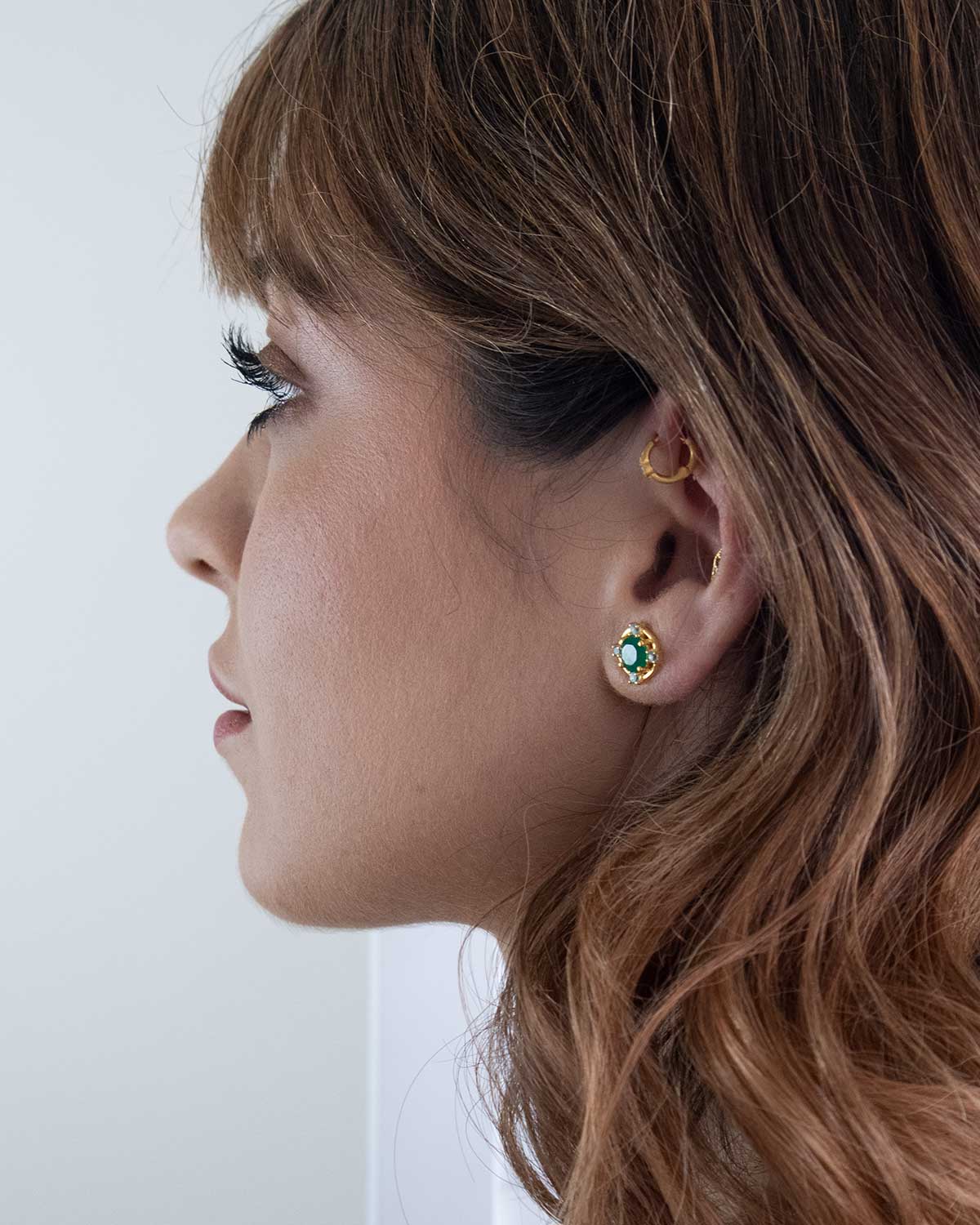 Model wearing gold stud earrings with green onyx and blue topaz