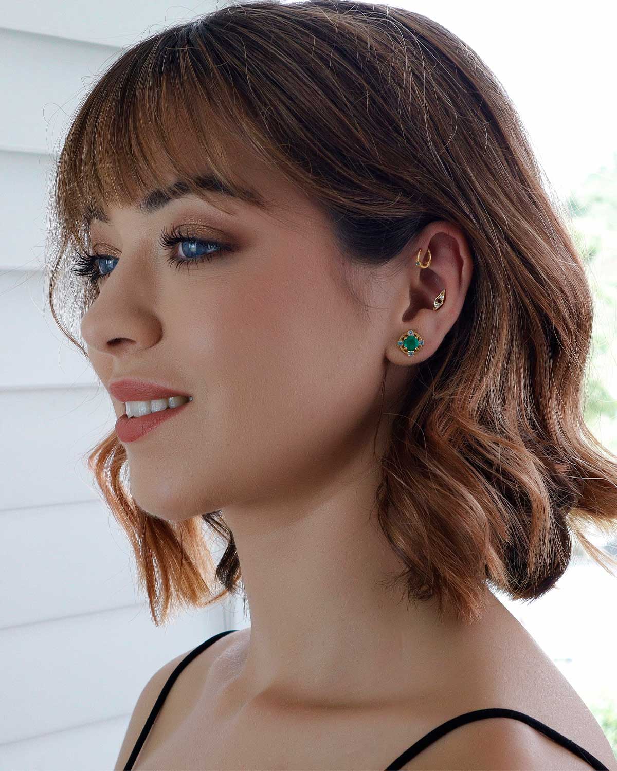 Side angle of gold stud earrings featuring green onyx and blue topaz