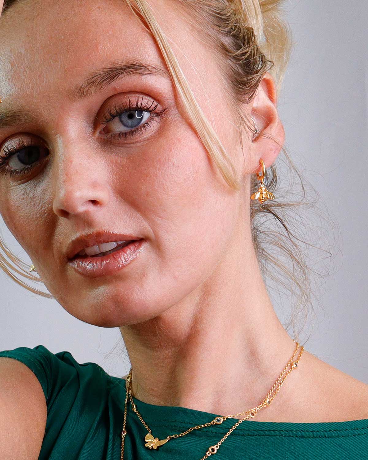 Model wearing gold mini hoop earrings with bee motifs for a subtle statement