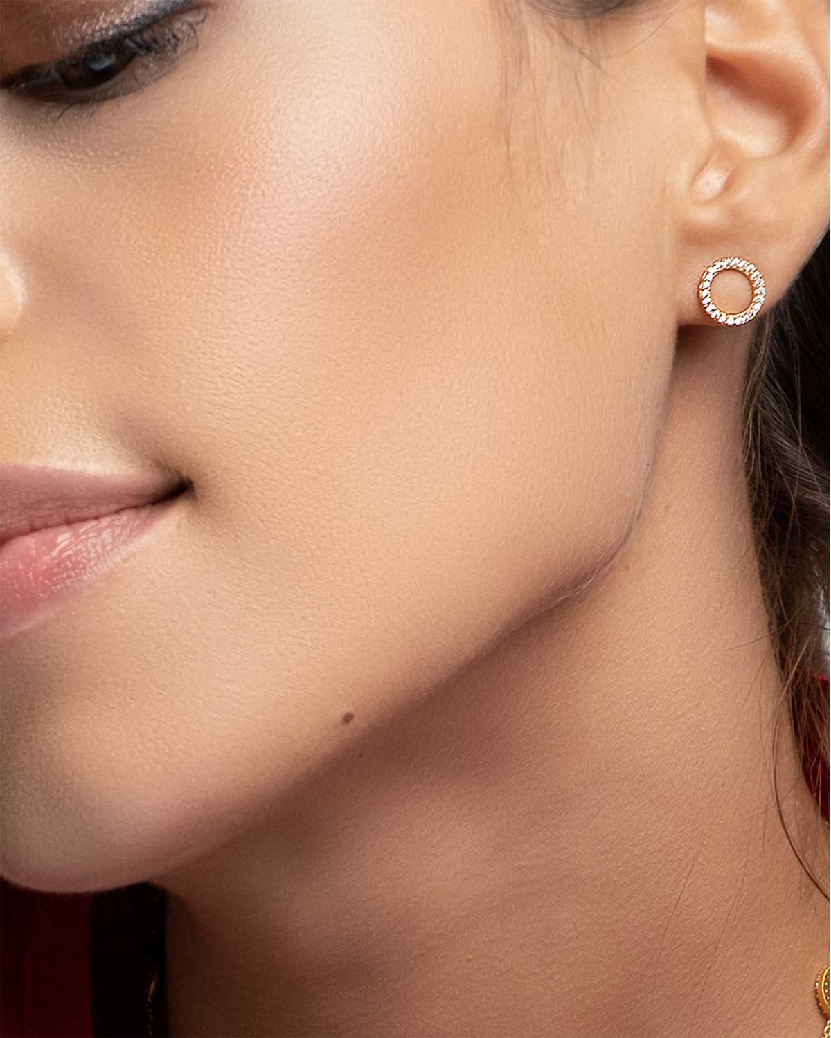 Model wearing circular gold stud earrings with crystal details