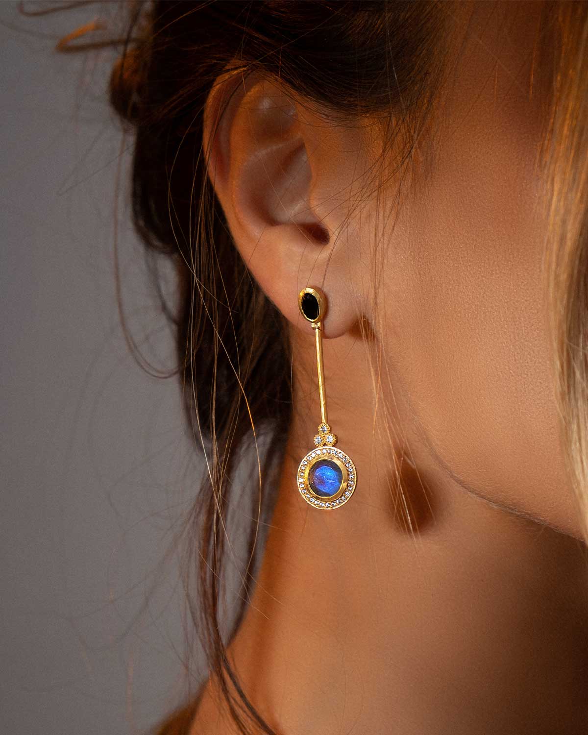 Model wearing gold earrings with flowing labradorite gemstones