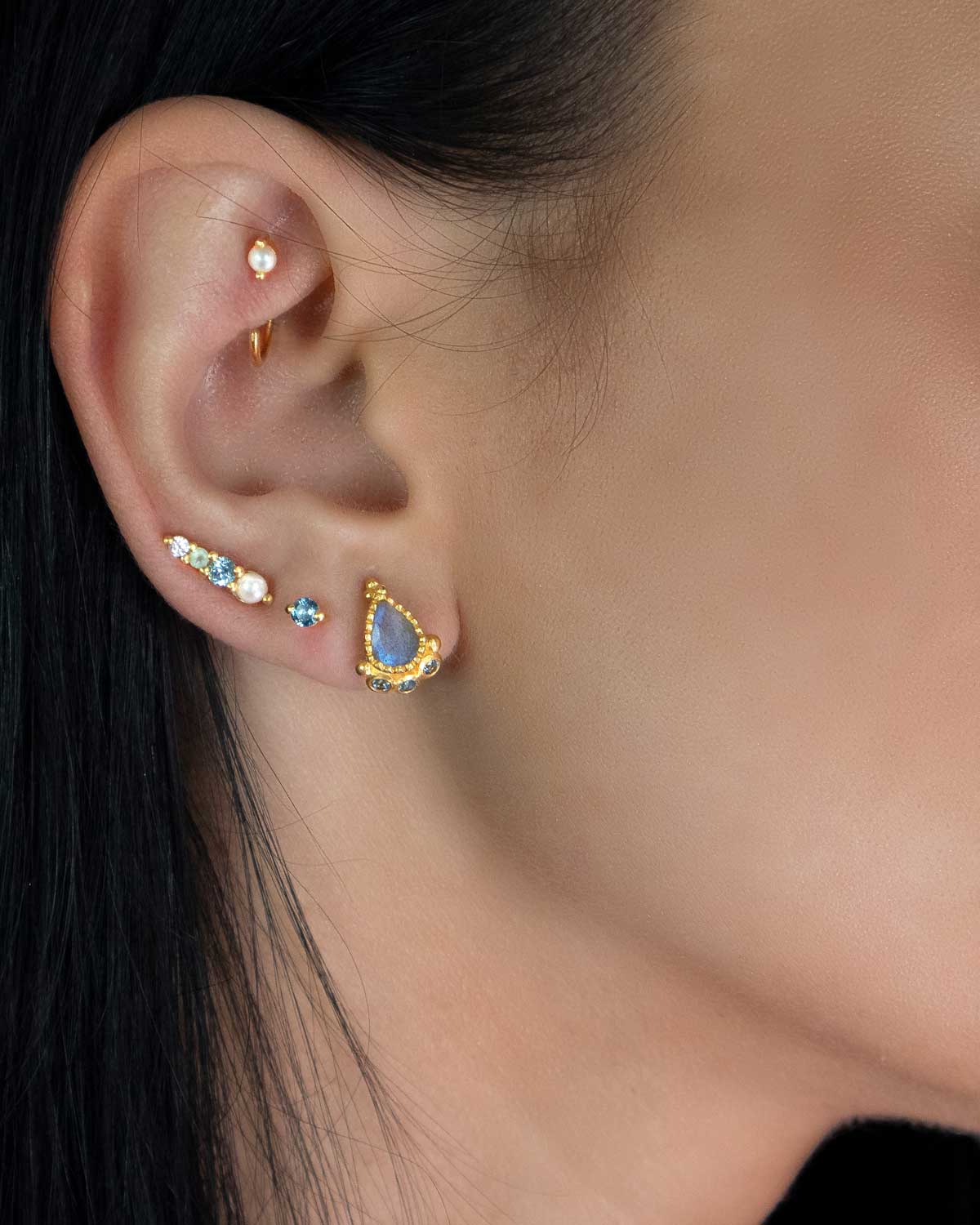 Model wearing mini gold studs with blue topaz and pearl accents