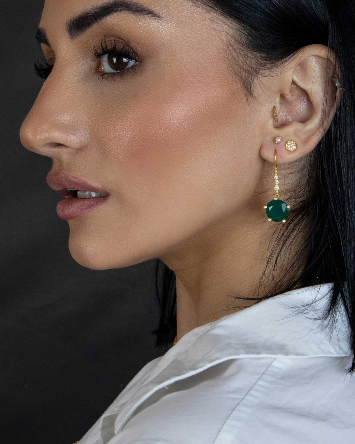 Close-up of gold earrings with emerald green onyx gemstones